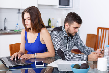 Young woman using laptop and man with phone at home kitchen