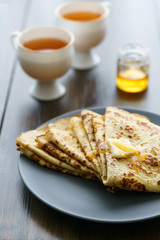 Crepes on a grey ceramic plate served with honey and 2 cups of tea. Dark wooden table, high resolution