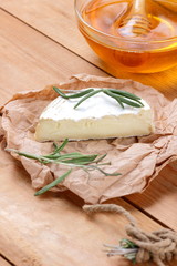 Camembert with rosemary branches on wooden boards. Soft cheese on parchment paper. Cheese with and honey on wooden background