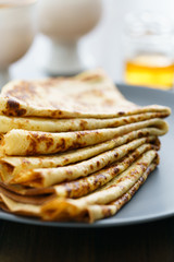 Crepes on a grey ceramic plate served with honey and 2 cups of tea. Dark wooden table, high resolution