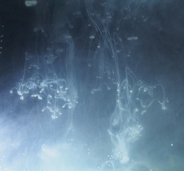 A drop of paint dissolves in water. On black background.