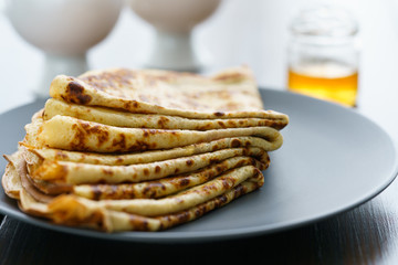 Crepes on a grey ceramic plate served with honey and 2 cups of tea. Dark wooden table, high resolution