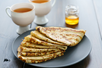Crepes on a grey ceramic plate served with honey and 2 cups of tea. Dark wooden table, high resolution