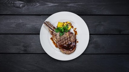 Rib-eye steak with corn rotating on a white plate. Top view on black wooden background