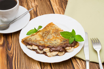 Crepes with bananas and cream on a wooden background