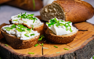 French Baguette with white curd spread decorated with green fresh chive served on wooden plate
