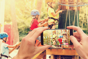 use mobile phone and blurred image of children climb on the rope net in the playground in the evening
