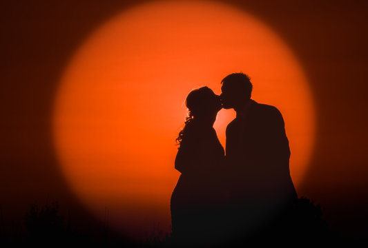 Silhouette photo of a young couple kissing at sunset on their wedding day - Sun in the background