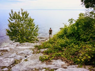 A man standing by the shore of Lake Ontario in Oakville, Ontari, Canada, staring out at the vast waters of the great lake deep in thought.