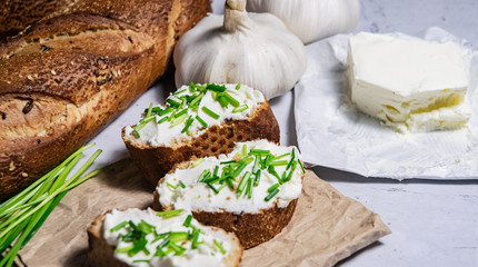Pieces of French baguette with fresh green chives, white curd spread placed on rustic paper