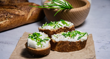 Pieces of French baguette with fresh green chives, white curd spread placed on rustic paper
