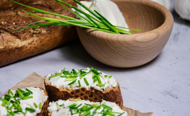 Pieces of French baguette with fresh green chives, white curd spread placed on rustic paper