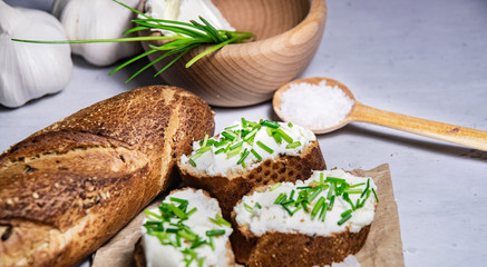 Pieces of French baguette with fresh green chives, white curd spread placed on rustic paper