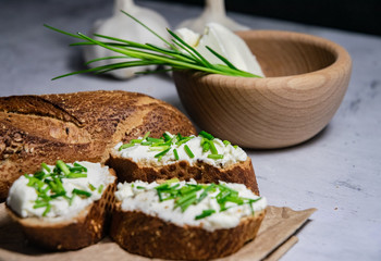 Pieces of French baguette with fresh green chives, white curd spread placed on rustic paper