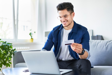 Portrait of handsome young man paying online with credit card and laptop while sitting at home