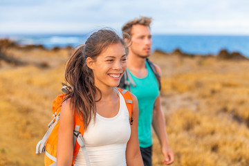 Fototapeta na wymiar Happy young couple tourists in love holding hands walking on trek hike with backpacks. Hikers on nature travel hiker trail destination smiling happy. Interracial relationship.