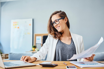 Cheerful young woman working with laptop and documents