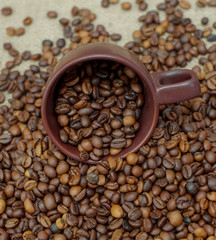 A cup of coffee full of coffee beans. Coffee cup and coffee beans. Grain coffee on burlap.
