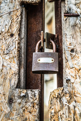 Abandoned building, with a fiberboard gate closed with a padlock in the foreground - focus on the padlock - obrazy, fototapety, plakaty