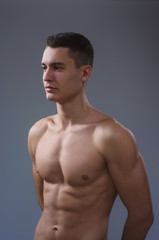 Fototapeta premium Beautiful young European athletic with bare torso, nice abs and muscles on white and gray background