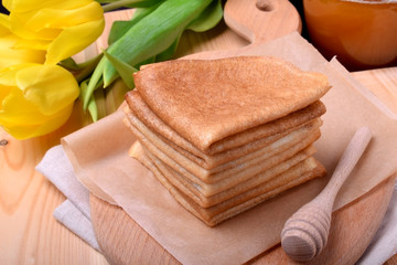 Stack of golden crepes on a wooden board and a honey spoon