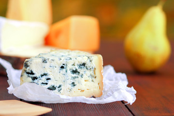 Various types of cheese and pear on wooden boards. Slices of cheese on blurred background. Dorblu, camembert and hard yellow cheese on parchment paper