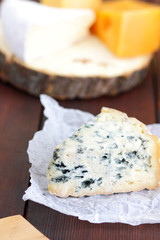 Various types of cheese and pear on wooden boards. Slices of cheese on blurred background. Dorblu, camembert and hard yellow cheese on parchment paper