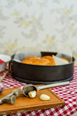 Garlic slices on the board, garlic press on the background of bread in the form and on a red and white napkin. Homemade bread, homemade baking.