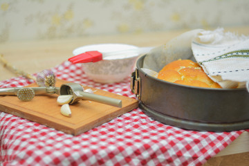 Garlic slices on the board, garlic press on the background of bread in the form and on a red and white napkin. Homemade bread, homemade baking.