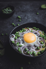 Creamy green pea soup with fried egg and red onion in black bowl, close up.