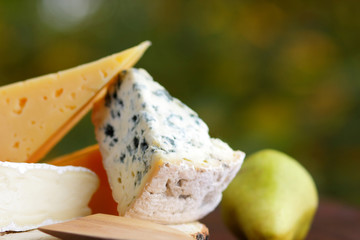 Various types of cheese and pear on wooden boards. Slices of cheese on blurred background. Dorblu, camembert and hard yellow cheese