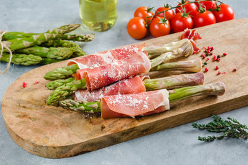 Fresh organic asparagus wrapped in Prosciutto ham on a cutting board.