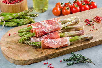 Fresh organic asparagus wrapped in Prosciutto ham on a cutting board.