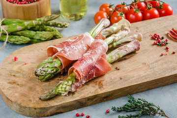 Fresh organic asparagus wrapped in Prosciutto ham on a cutting board.
