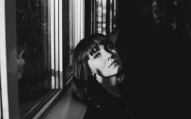 Beautiful model laying her head upon the window sill of a greenhouse building. Pale white face of a...