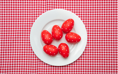 Easter eggs, red with dots, in a white plate, red checkered tablecloth background