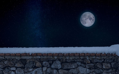 Stone wall covered by fresh snow during a winter. A starry sky with the full Moon appears in the background. Elements of this image furnished by NASA.