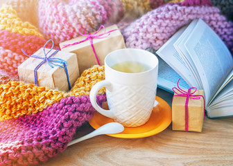 A сup of tea, wrapped gifts and an open book on the background of a knitted blanket.