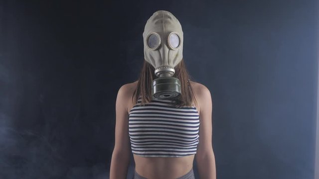 Portrait of woman in a gas mask in smoky dark room.