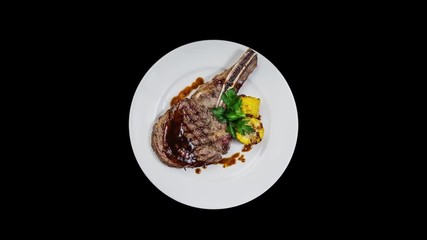 Rib-eye steak with corn rotating on a white plate. Top view, Isolated on the black background.