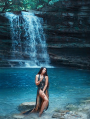Georgia magic nature in Martvili Canyon, dark-haired sexy girl comes out of the azure transparent clear waterfall lake water, sea nymph in gorgeous green dress with deep neckline and cuts on train