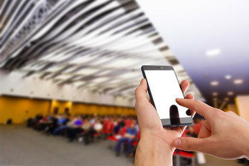 Man use mobile phone, blur image of people live in large conference room as background.