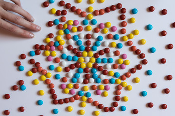 A hand pulls for colorful chocolate coated candy on white background. Unhealthy nutrition concept