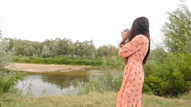 A brunette girl with long hair photographs the river. Slow motion. Beautiful landscape