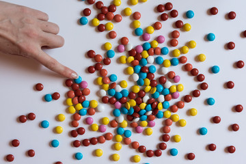 A hand pulls for colorful chocolate coated candy on white background. Unhealthy nutrition concept