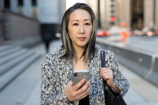 Asian woman in city walking texting cell phone