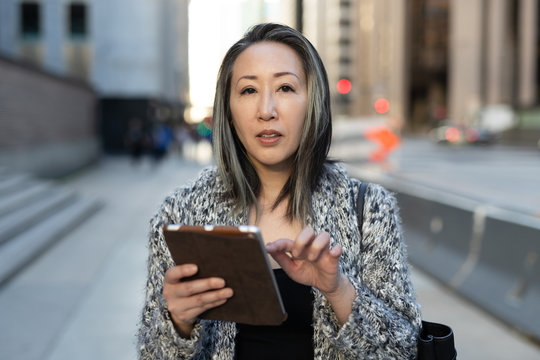 Asian woman in city walking using tablet computer
