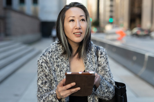 Asian woman in city walking using tablet computer