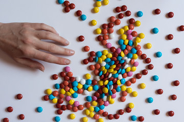 A hand pulls for colorful chocolate coated candy on white background. Unhealthy nutrition concept