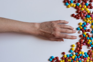 A hand pulls for colorful chocolate coated candy on white background. Unhealthy nutrition concept